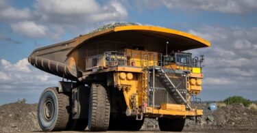 A yellow haul truck parked in the middle of a construction site. There are large mounds of dirt in the background.