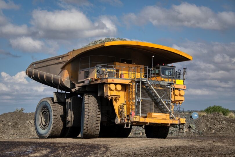 A yellow haul truck parked in the middle of a construction site. There are large mounds of dirt in the background.