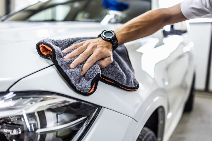 A man wipes down his white, sparkling clean car with a microfiber cloth to detail it on a budget.