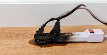 A close-up of an electrical surge protector outlet and extension cord that was on fire and burnt to a crisp.
