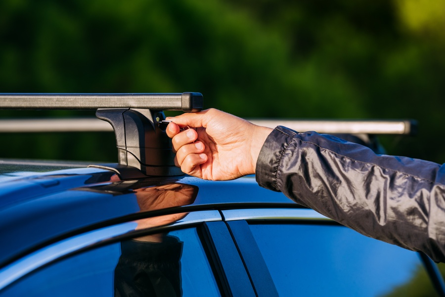 A close-up view shows a person wearing a black jacket using a key to lock the black roof rack on top of the vehicle.