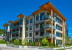 The exterior of a modern apartment building with balconies, wood accents, and landscaping on a sunny day.