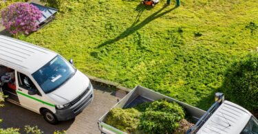 A professional landscaper mows the lawn of a business. There are two trucks parked near the lawn, one carries the brush.
