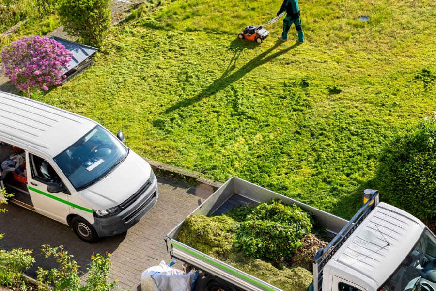 A professional landscaper mows the lawn of a business. There are two trucks parked near the lawn, one carries the brush.