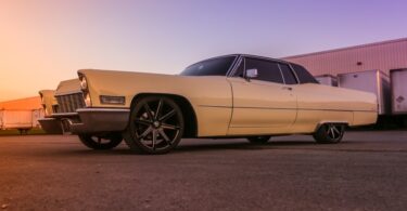 A full side view of a classic Cadillac low rider car with two doors, a black top, and cream exterior color.