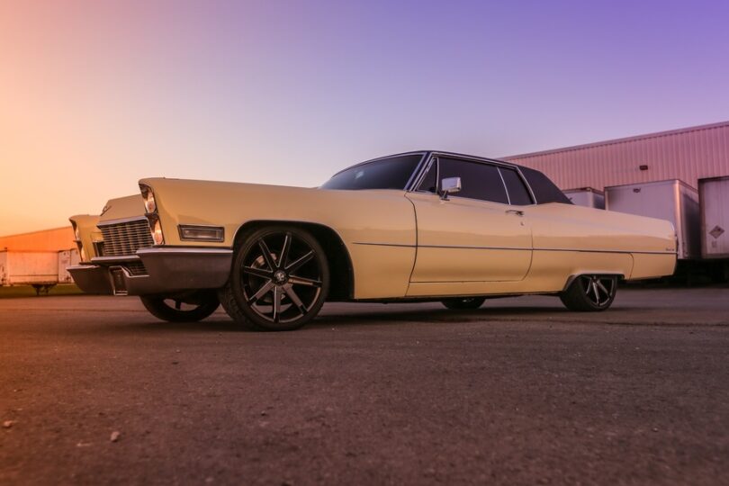 A full side view of a classic Cadillac low rider car with two doors, a black top, and cream exterior color.