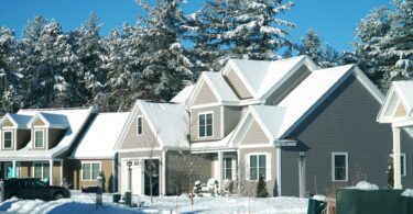 A row of houses covered in snow after a blizzard. There is snow on the lawn and on the trees behind the homes.