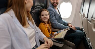 Cheerful little girl traveling with parents on an airplane. She's flipping through an airplane magazine.