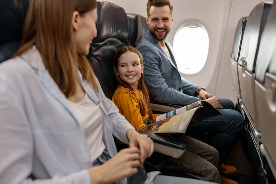 Cheerful little girl traveling with parents on an airplane. She's flipping through an airplane magazine.