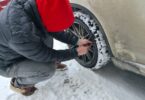 A man wearing multiple layers to stay warm while inflating his car tire. The tire tread is covered in snow.
