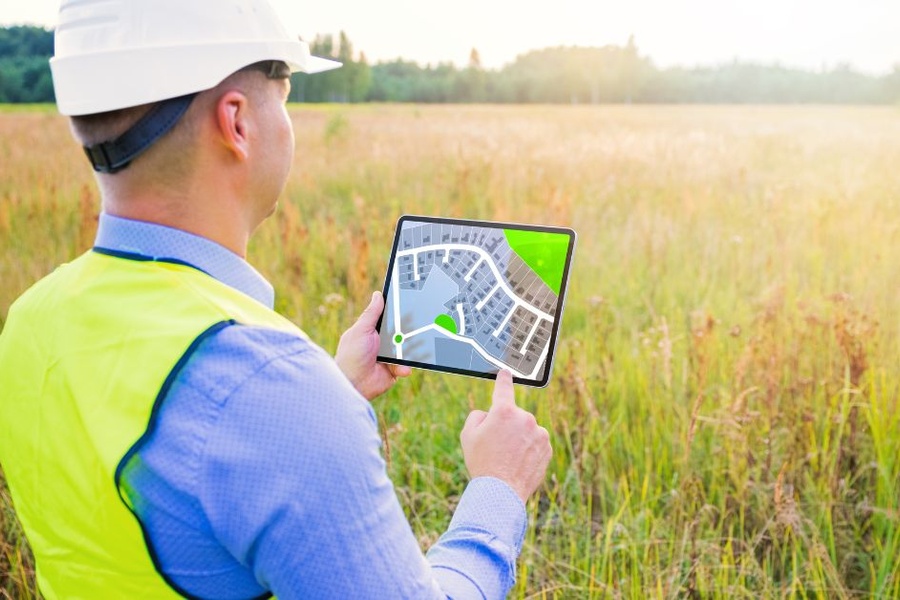 A land inspector looks out over a plot of overgrown land. He has a tablet in his hand depicting housing zones.