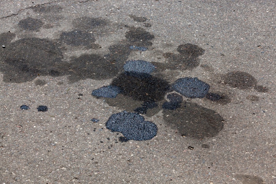 Several puddles of black oil on the road. The sun shines down on the puddles, and some puddles are drier than others.