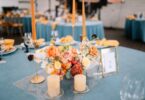 A centerpiece on a table for a rehearsal dinner. There are orange candles and an arrangement of flowers in the center.