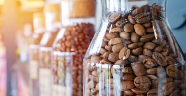 Glass carafes sit on a counter together in a row. Each one is full of fresh coffee beans with a cork topper.