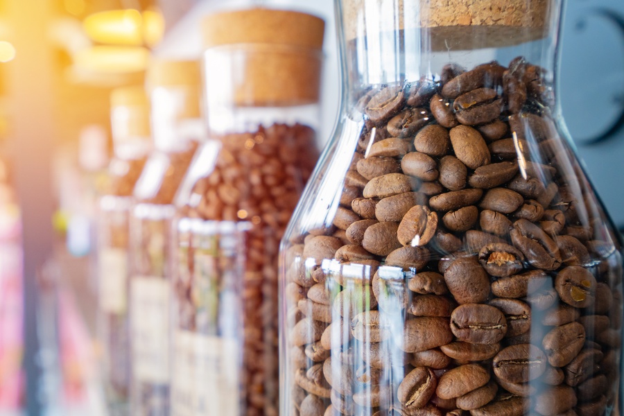 Glass carafes sit on a counter together in a row. Each one is full of fresh coffee beans with a cork topper.