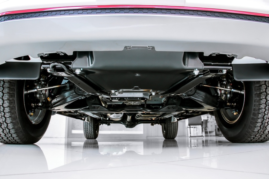 A bottom view of a car’s suspension and chassis featuring clean metal surfaces, parked inside a bright facility.