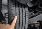 A close-up of a person pointing their finger at the tire wear indicators on a car tire attached to a car on a lift.