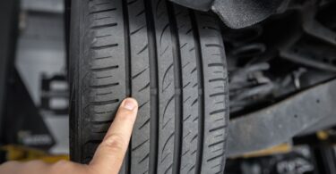 A close-up of a person pointing their finger at the tire wear indicators on a car tire attached to a car on a lift.