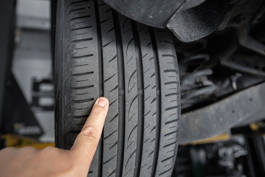 A close-up of a person pointing their finger at the tire wear indicators on a car tire attached to a car on a lift.