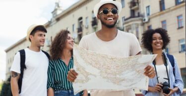 Group of young travelers exploring a city together while smiling and looking at a map during a sightseeing trip
