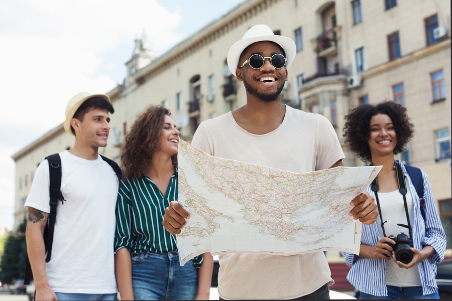 Group of young travelers exploring a city together while smiling and looking at a map during a sightseeing trip