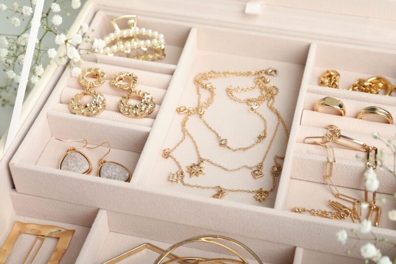An open jewelry organizer with gold necklaces, rings, and earrings neatly arranged in soft compartments.