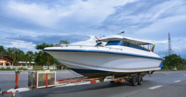 A white boat with small rainbow stripes on the hull is attached to a trailer for transport.