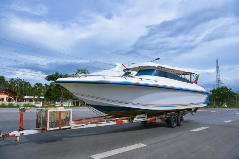 A white boat with small rainbow stripes on the hull is attached to a trailer for transport.