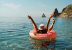 A woman raising her hands and feet into the air while lounging in an inflatable tube on the ocean water.