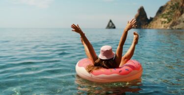 A woman raising her hands and feet into the air while lounging in an inflatable tube on the ocean water.