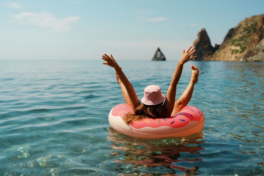 A woman raising her hands and feet into the air while lounging in an inflatable tube on the ocean water.