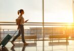 Young woman walks by an airport window hauling a suitcase, waiting to board a plane at the terminal gate.