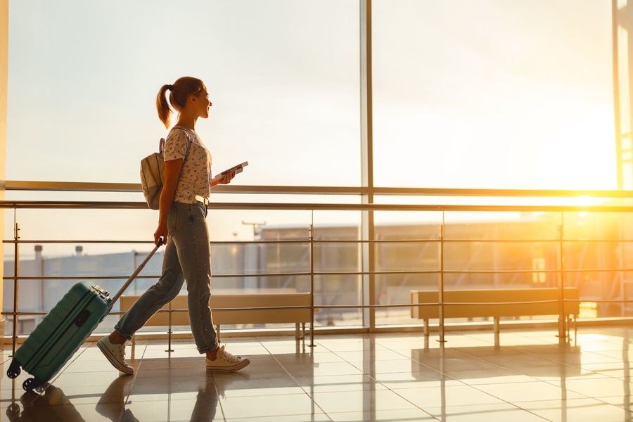 Young woman walks by an airport window hauling a suitcase, waiting to board a plane at the terminal gate.