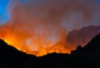 A mountain range is in the background and in the foreground there is a fire blazing. Smoke is rising from the fire.