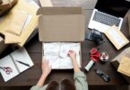 Someone stands at a desk with packaging supplies. They have an open product box with twine and a "thank you" card inside.