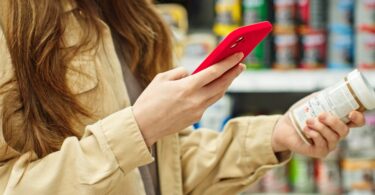 A woman holding her phone in one hand and using it to compare prices of the pill bottle in her other hand.