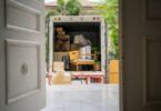A view through a front door into the back of a moving truck. The truck is filled with boxes and pieces of furniture.