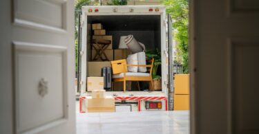 A view through a front door into the back of a moving truck. The truck is filled with boxes and pieces of furniture.