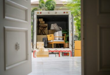 A view through a front door into the back of a moving truck. The truck is filled with boxes and pieces of furniture.