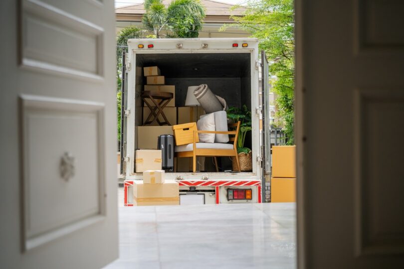 A view through a front door into the back of a moving truck. The truck is filled with boxes and pieces of furniture.