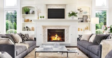 A luxurious living room and fireplace with multiple couches and large windows in the corner of the room.