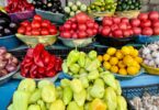 a farmer's market display with tomatoes, peppers, eggplants, cucumbers, lemons, onions, and garlic in baskets.