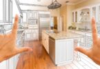 Two hands framing a kitchen design blending a design drawing with finished cabinets and kitchen appliances.