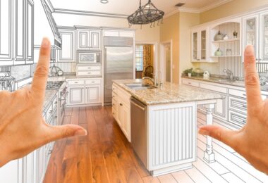 Two hands framing a kitchen design blending a design drawing with finished cabinets and kitchen appliances.