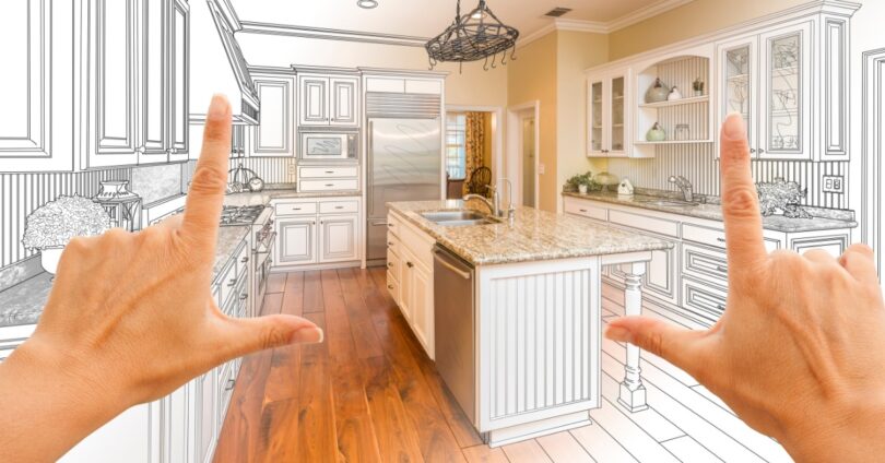 Two hands framing a kitchen design blending a design drawing with finished cabinets and kitchen appliances.
