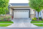 A view from the street of a house's garage with a white door. There is a concrete driveway leading up to the door.