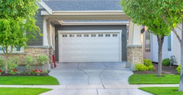 A view from the street of a house's garage with a white door. There is a concrete driveway leading up to the door.