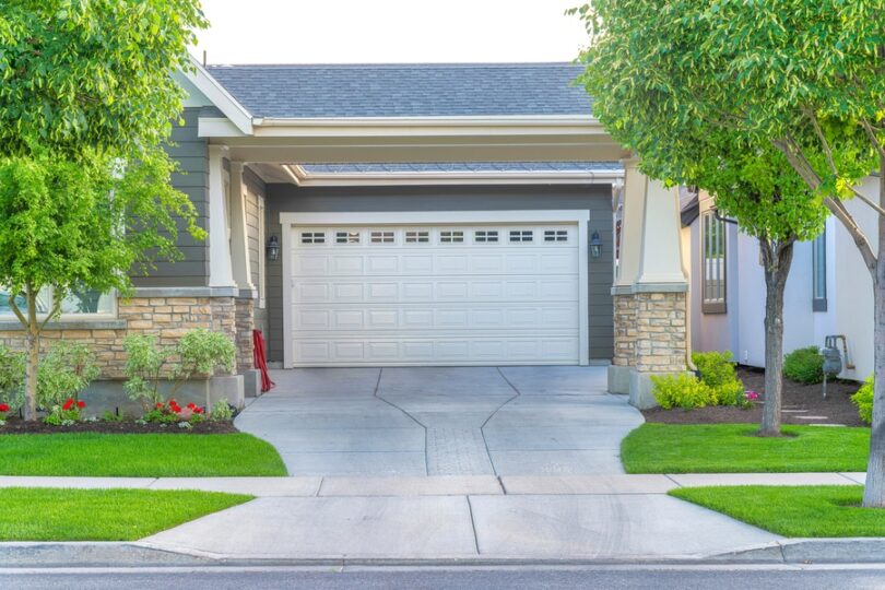 A view from the street of a house's garage with a white door. There is a concrete driveway leading up to the door.