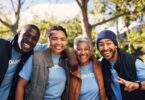 A group of male and female adults in matching blue T-shirts that say "VOLUNTEER" smiling and posing outside together.