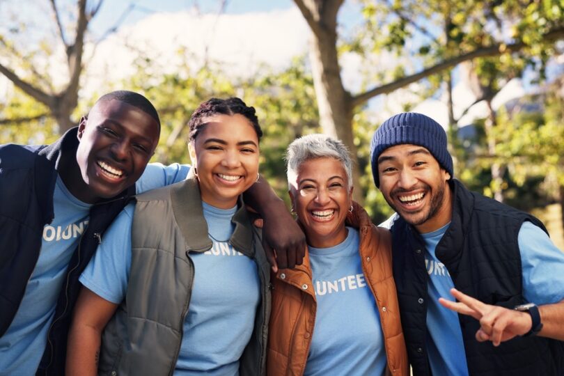 A group of male and female adults in matching blue T-shirts that say "VOLUNTEER" smiling and posing outside together.
